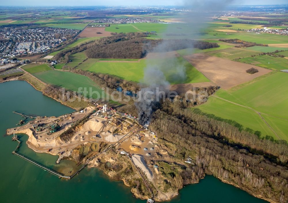 Pulheim aus der Vogelperspektive: Rauch- und Flammenbildung während der Löscharbeiten zum Brand einer Lagerhalle des Terra Kieswerkes am Ufer des Pullheimer See in Pulheim im Bundesland Nordrhein-Westfalen