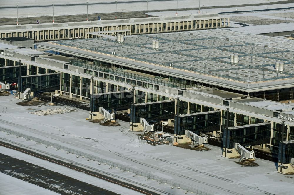 Schönefeld aus der Vogelperspektive: Winterlich schneebedeckte Abfertigungs- Gebäude und Terminals auf dem Gelände des Flughafen in Schönefeld im Bundesland Brandenburg