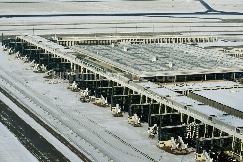 Luftaufnahme Schönefeld - Winterlich schneebedeckte Abfertigungs- Gebäude und Terminals auf dem Gelände des Flughafen in Schönefeld im Bundesland Brandenburg